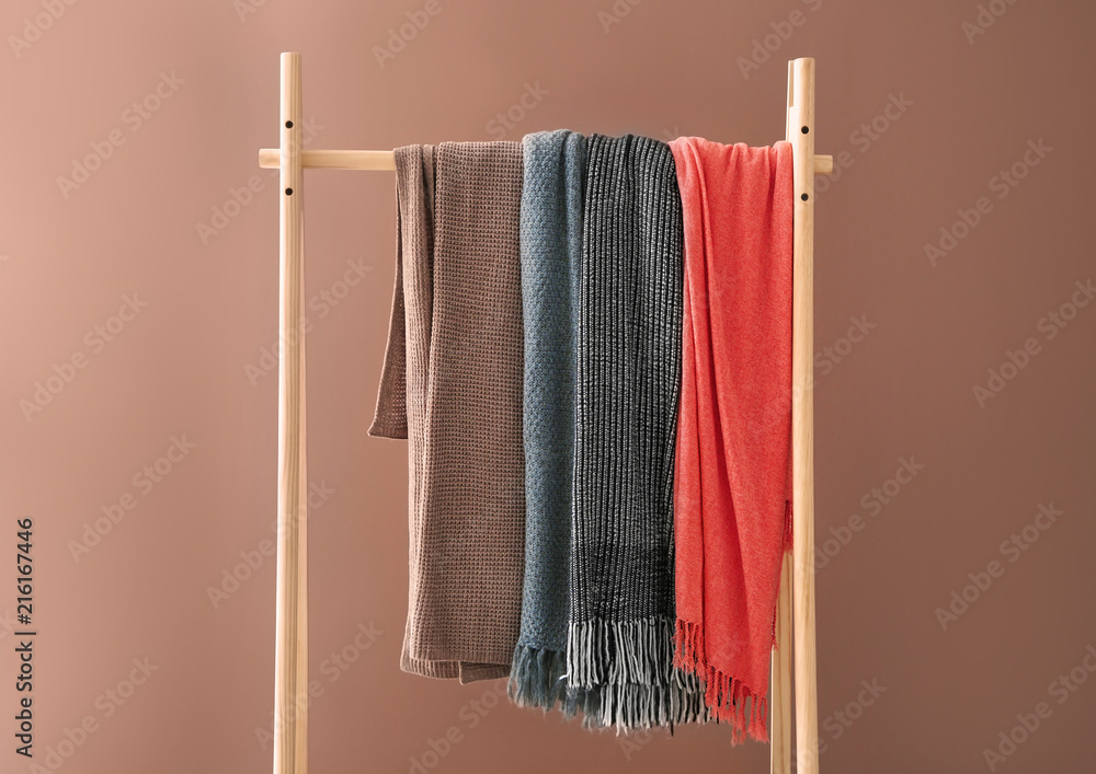 Wooden rack with warm plaids on color background