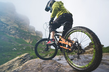 Legs Of Bicyclist And Rear Wheel Close-up View Of Back Mtb Bike In Mountains Against Background Of Rocks In Foggy Weather. The Concept Of Extreme Sports