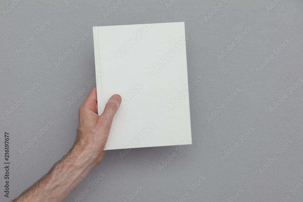 Male hand holding a closed book showing the book cover. Book Mock up template. - obrazy, fototapety, plakaty 