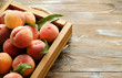 Bunch of ripe organic peaches in pile on wooden tray with rope handles on grunged wood textured table. Local produce harvest heap. Clean eating concept. Background, top view, close up, copy space