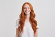 Portrait of cheerful cute redhead young woman with long wavy hair and freckles wears stylish t shirt looks relaxed and laughing isolated over white background Feels happy