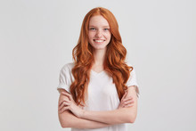Closeup Of Happy Confident Young Woman With Long Wavy Red Hair And Freckles Wears T Shirt Keeps Arms Crossed And Looks Directly In Camera Isolated Over White Background