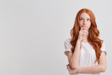 Closeup of cute thoughtful redhead young woman with long wavy hair and freckles wears stylish t shirt thibnking and planning her working day isolated over white background