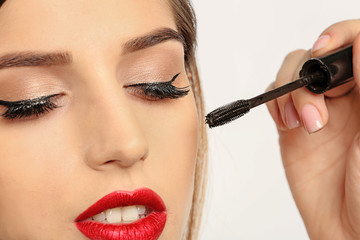 Beautician applying mascara on young woman's eyelashes against white background