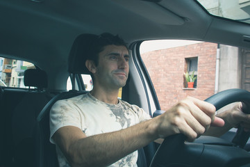 Young man driving car on urban city. Smiling driver holding steering wheel with no seat belt on. Road trip, auto rental, insurance, traffic ticket, irresponsible concepts