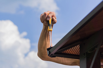 screwdriver in males hands. Worker with a hand tool assembling metal construction outdoors