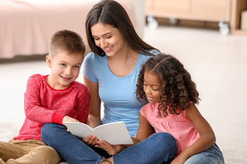 Canvas Print - Young woman reading book to little kids indoors. Child adoption