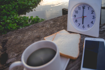 Wall Mural - Coffee bread and White clock on a wooden table in the morning.On the river at 6:00 pm, there is a white clock on the wooden floor.Smartphone put on table.Do not focus on objects.Warm tone.