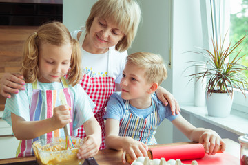 Happy grandmother with her grandchildren having fun during baking muffins and cookies