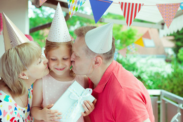 Wall Mural - Portrait of happy grandparents celebrating birthday with their pretty little granddaughter on decorated terrace