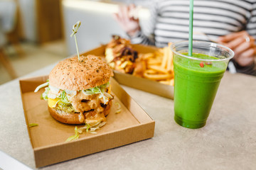 A young woman drinks green smoothies and eats a burger in a vegan fast food restaurant