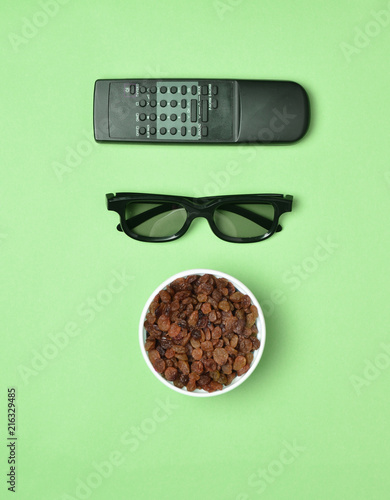 Fotografia, Obraz 3d glasses, tv remote, bowl with raisins on pink pastel background, top view