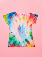 T-shirt Painted In Tie Dye Style On A Pink Background. Flat Lay. Pastel Color.