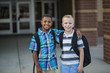 © Brocreative - Portrait of Two diverse school kids standing outside their elementary school building. Back to school photo of diverse school kids wearing backpacks in the school yard