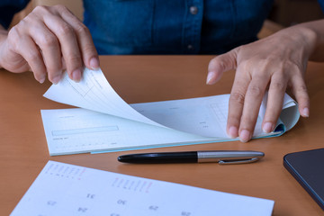 Wall Mural - Business woman hand pullingout a check from cheque book after signing and writing, working at office with calendar and pen on the wooden table.