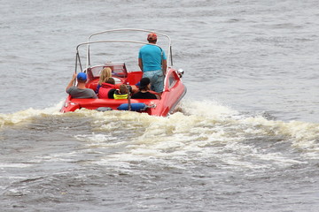 Wall Mural - Travel, water activities - red 18-ft motor boat with passengers slowly floating away on the water, rear view