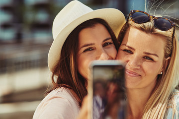 Wall Mural - Two smiling female friends taking selfie together outside in sum