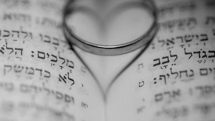 Close up of the Hebrew Jewish bible with a weeding ring creating a heart shape shadow 