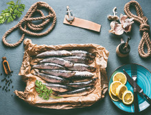 Raw Sardines On Kitchen Table Background With Ingredients . Lemon, Garlic And Herbs For Tasty Seafood Cooking. Cooking Preparation Of Fishes