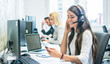 © Bojan - Friendly female customer support operator with headset using phone in office