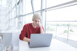 © bodnarphoto - Concentrated young businessman in casual clothing, sitting at a table at the coworking window and working on a laptop. Young man uses a laptop in a cafe. Portrait of a freelancer at work