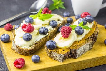 Wall Mural - Traditional American and European summer breakfast: sandwiches of toast with peanut butter or cream cheese with raspberries and blueberry, banana. Black concrete table. copy space top view