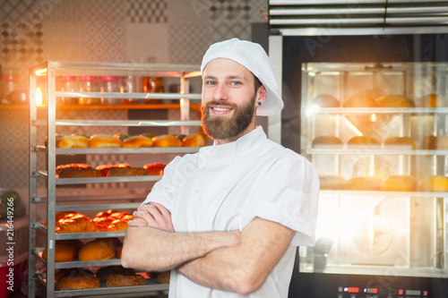 Fotografie, Obraz Portrait of a young beautiful baker with fresh bread and an oven in the backgrou