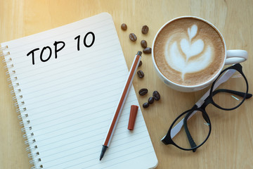 Top 10 word on notebook with glasses, pencil and coffee cup on wooden table. Business, internet, education, technology concept.