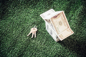 Model money house and key on green artificial grass with blue sky background.