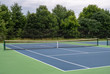 Small, blue asphalt neighborhood tennis court surrounded by green