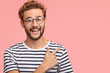 © wayhome.studio - Attractive unshaven man with curly hairstyle, looks positively at camera as indicates at blank space for advertising content, isolated over pink studio wall. Hey, look here! Cheerful hipster indoor