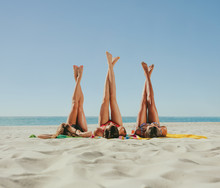 Woman In Bikini Sunbathing On Beach With Legs Raised To The Sky