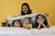 © Sirirat Makprasert - Babysitting playing with three foolish playful kids carrying on the bed; widow young woman and child are enjoying funny time indoor in modern yellow bed room.