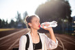 Portrait of beautiful girl in earphones drinking water on running track of stadium