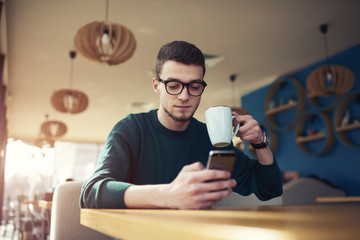 Attractive concentrated young student dressed in trendy pullover spending leisure time on break in cafeteria monitoring latest news on informational websites using free internet access in coffee shop