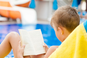 Wall Mural - Little boy reading a book by the pool.  Relaxation resting vacations concept