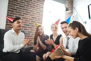 Poster - Joyous girl opening giftbox with birthday present from her friends at party while they clapping hands