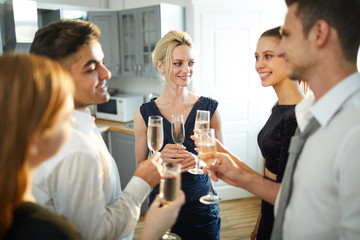 Poster - Group of young cheerful people with flutes of champagne making circle while talking and toasting at party