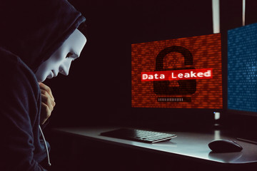 masked hacker under hood using computer to hack into system and employ data leaking process - intern
