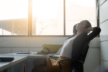 Businesswoman calm and smiling relaxing on her comfortable chair at the office. She satisfied after her work done, enjoying break with eyes closed, peace of mind with no stress.