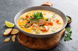 Salmon soup with cream, potatoes, carrots and parsley on gray background.