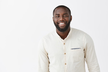 Charming dark-skinned boyfriend ready to make proposal, feeling happy and confident, dressing in white trendy shirt and smiling broadly at camera, practicing speech in front of mirror over gray wall