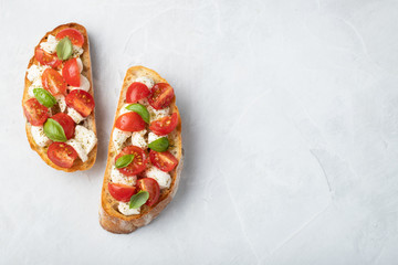 Bruschetta with tomatoes, mozzarella cheese and basil on a light background. Traditional italian appetizer or snack, antipasto. Top view with copy space. Flat lay