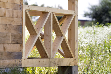 Wall Mural - Close-up section geometrical decorative simple detail of new natural not painted wooden planks and bars for balcony, attic fence on blurred blooming summer field background. Construction and design.