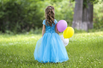 back view full-length portrait of pretty little blond long-haired girl in long blue dress with color