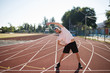 © Anton - Young sporty guy in cap thoughtfully looking aside while stretching on treadmill of stadium