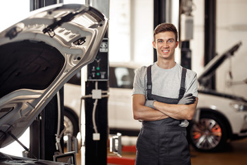 Wall Mural - A young and qulified automechanic is standing near the car at a 