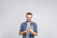 Happy young man in plaid shirt standing and using tablet over grey background