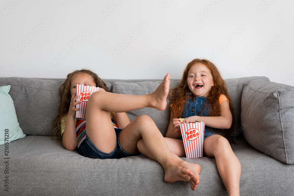 Smiling little girls on sofa watching TV while eating pop corn