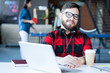 © Seventyfour - Portrait of smiling bearded man wearing headphones and glasses looking at camera while sitting at desk in modern office of IT developers company, copy space